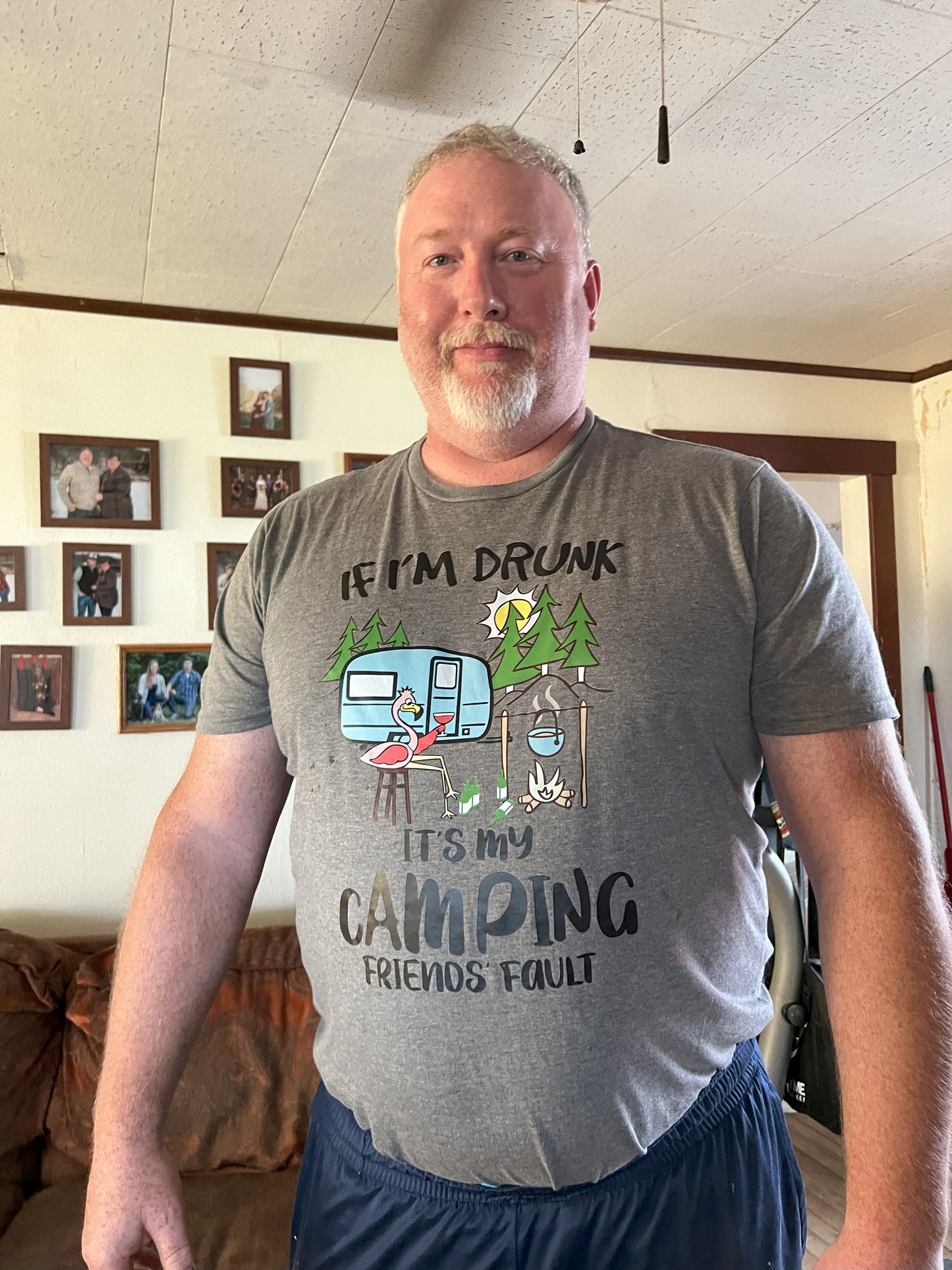 A person wearing a gray t-shirt with a humorous text-related graphic and statement 'IF I'M DRUNK, IT'S MY CAMPING FRIENDS' FAULT'.