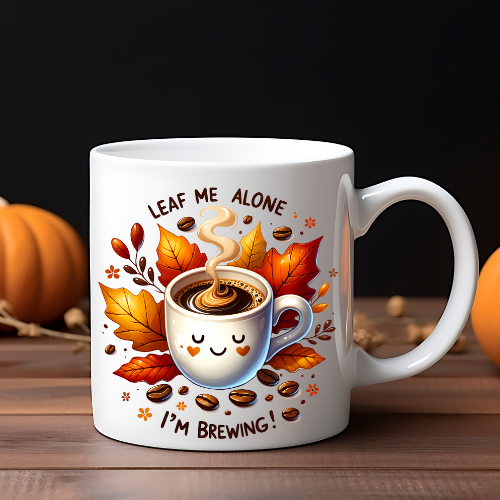 A white ceramic coffee mug with a leaf design and the text 'Leaf Me Alone I'm Brewing!' along with a graphic of a steaming mug with leaves.