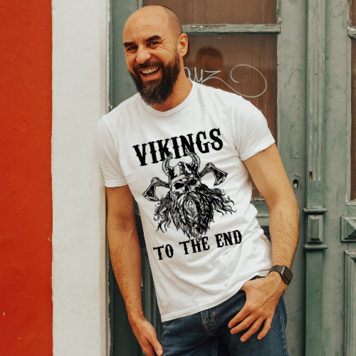 Man wearing a white t-shirt with 'Vikings to the End' design standing against a red and gray wall.