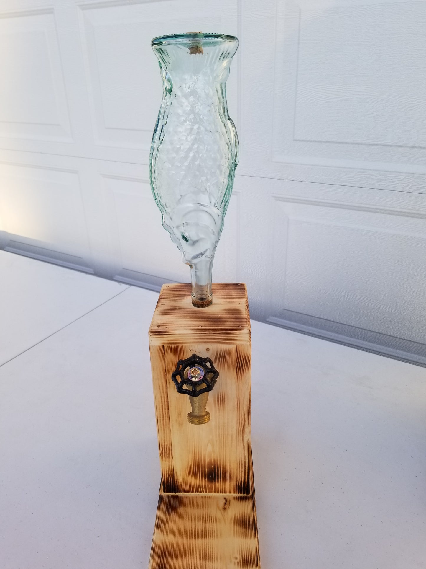 Rustic liquor dispenser with tall fish bottle, spigot, and refill funnel.