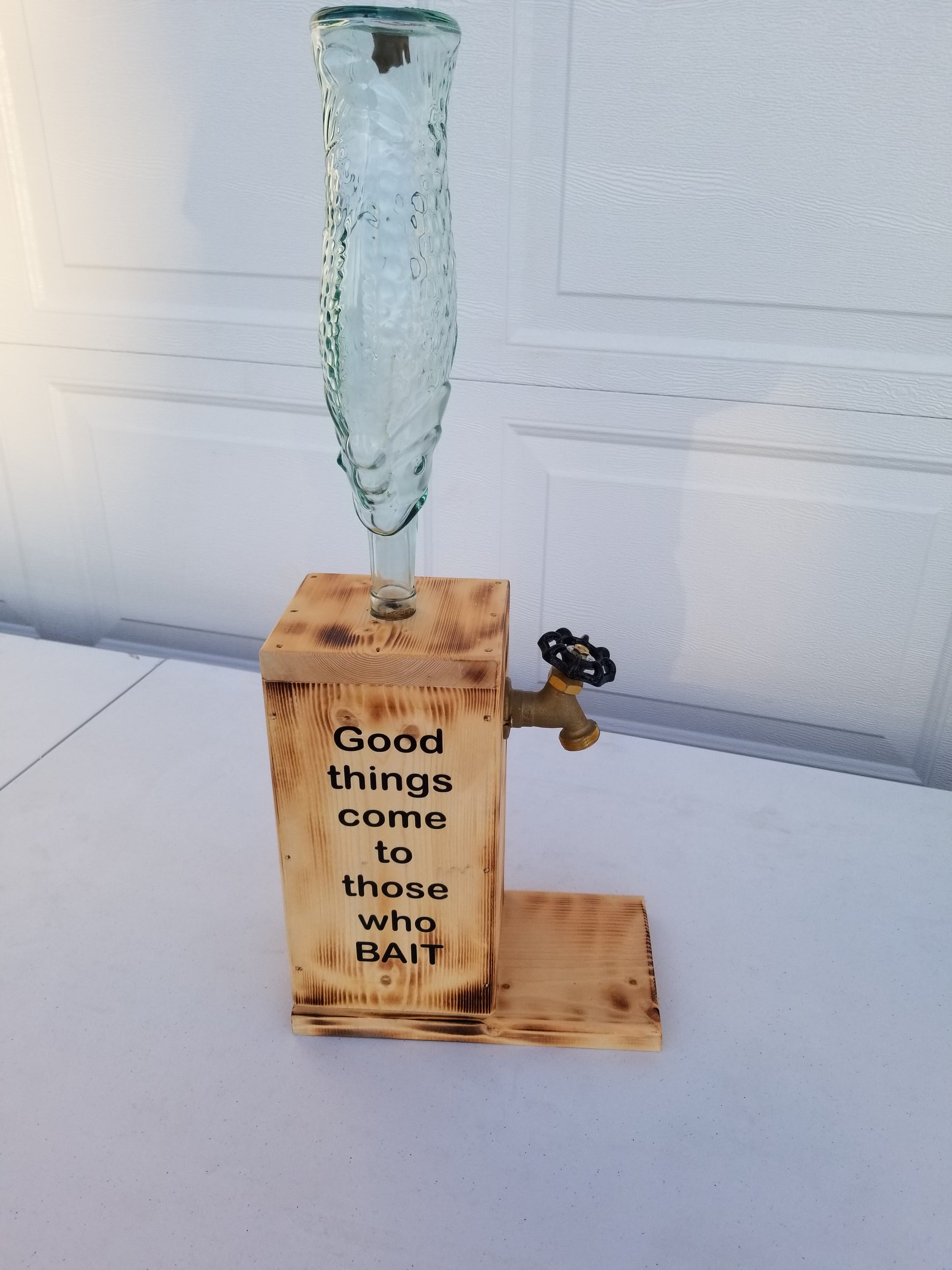 Rustic liquor dispenser with tall fish bottle, spigot, and refill funnel.