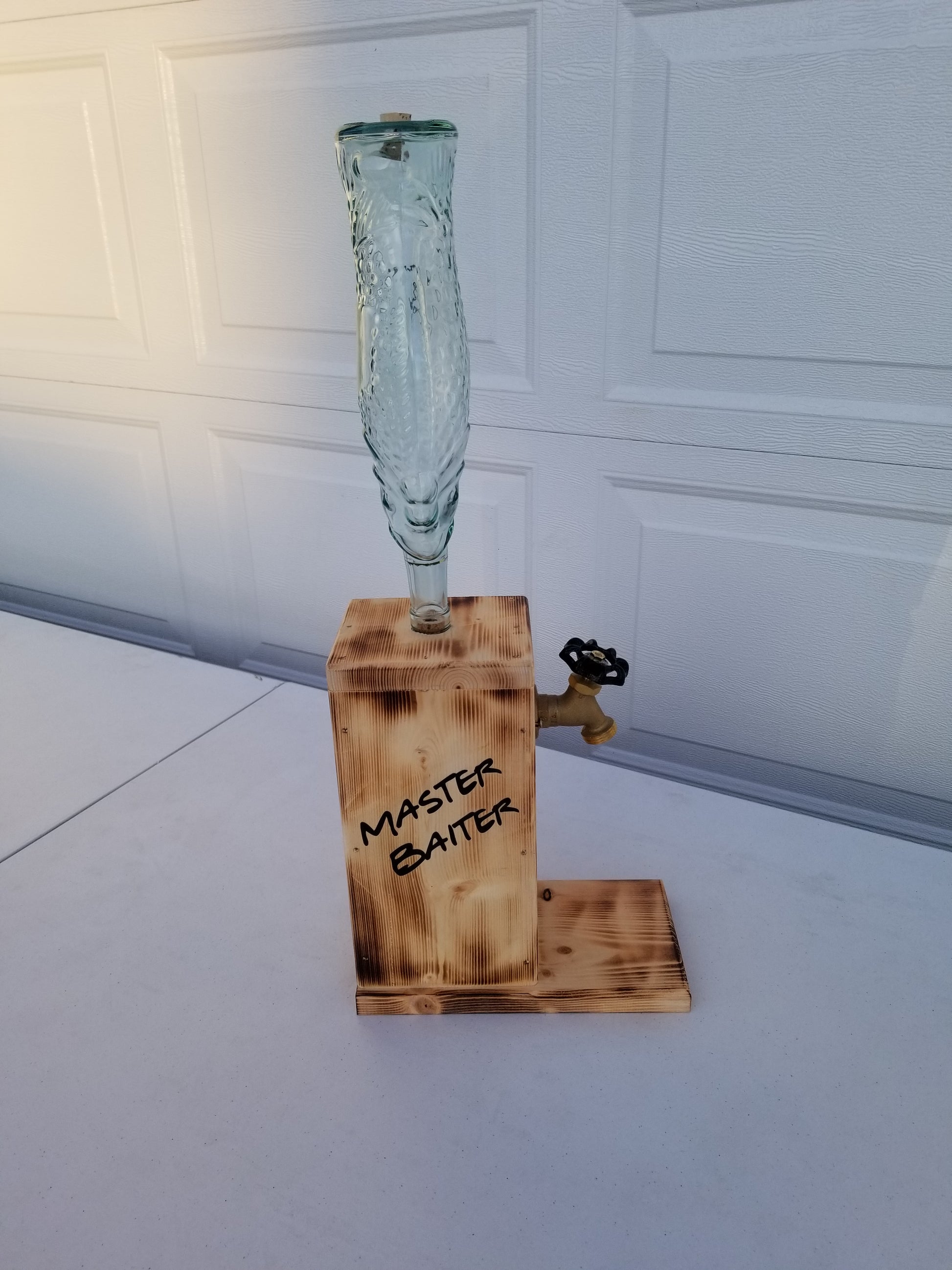 Rustic liquor dispenser with tall fish bottle, spigot, and refill funnel.