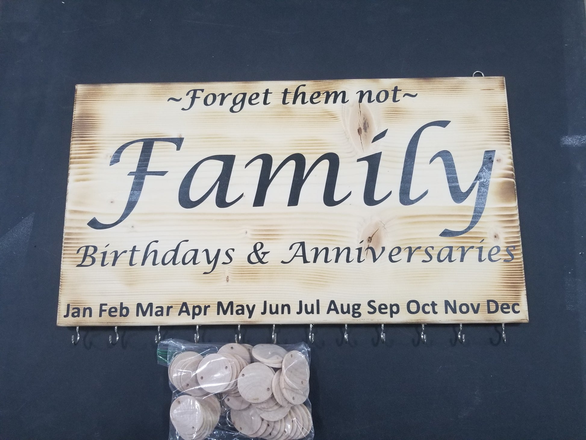 A wooden sign with the text 'Family Birthdays & Anniversaries' and hooks for hanging wooden discs, displayed with a bundle of wooden discs in front.
