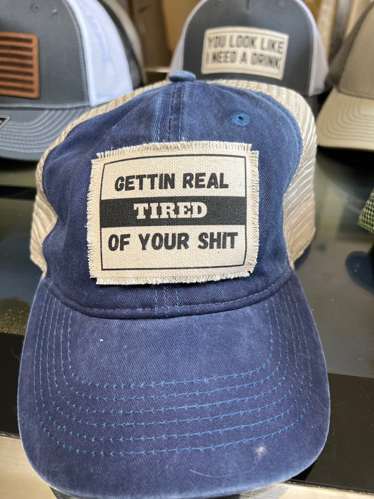 A blue denim snapback hat with text on it that reads 'GET REAL TIRED OF YOUR SHIT'.