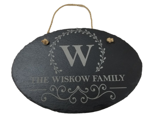 A slate door hanger with an engraved initial and the phrase 'THE WISKOW FAMILY' surrounded by a floral wreath design.