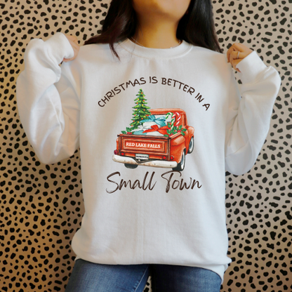 White sweatshirt with vintage red truck and Christmas tree design reading 'Christmas Is Better in a Small Town,' featuring customizable city and state license plate.