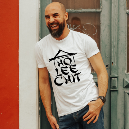 Man wearing a white t-shirt with black text, standing against a red and gray wall.