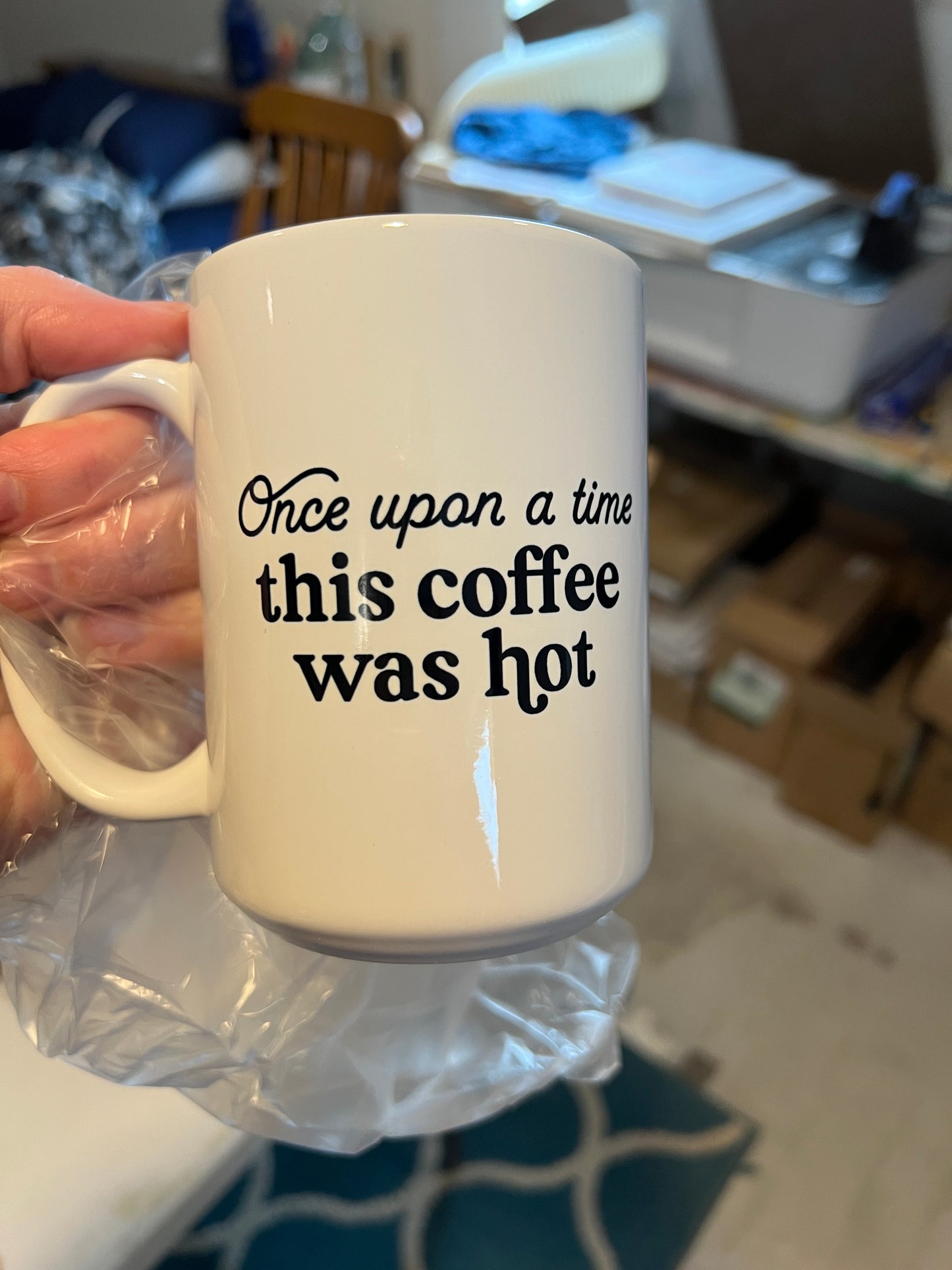 Mug with text 'Once upon a time this coffee was hot' held by a person in a casual setting.