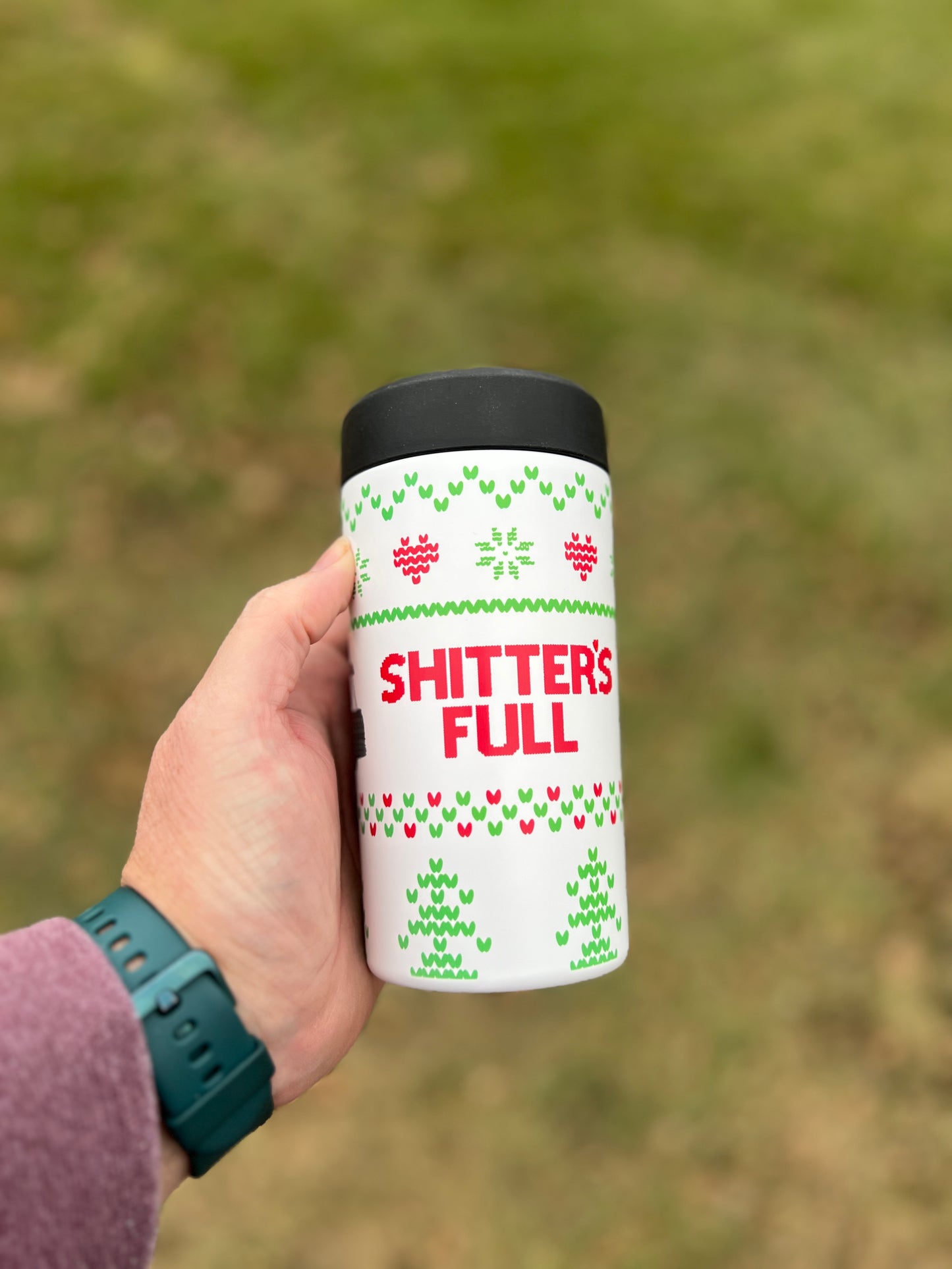 Hand holding a white tumbler with text and patterns against a blurred green background