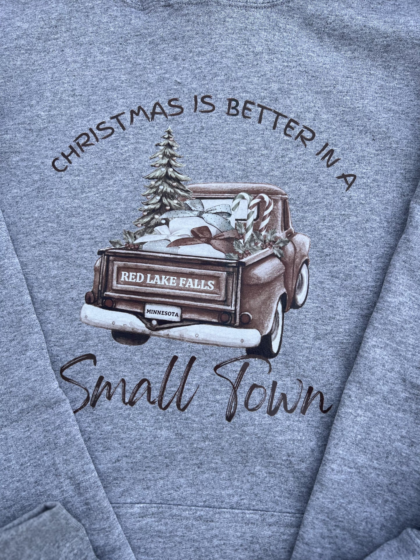 Gray sweatshirt with a graphic of a truck and text 'Christmas is better in a small town' on a blue background