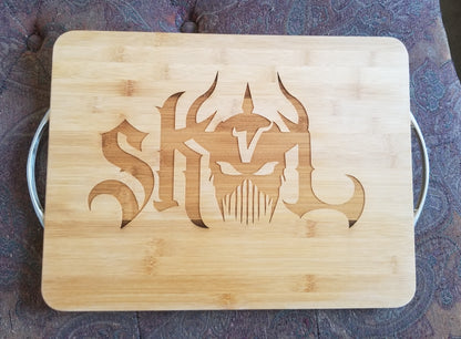 A bamboo cutting board with handles, featuring a stylized animal (bull) and text ('SKOL') design on the surface.